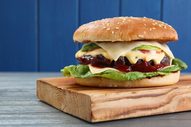 Photo of Tasty homemade cheeseburger with lettuce on grey wooden table, closeup. Space for text