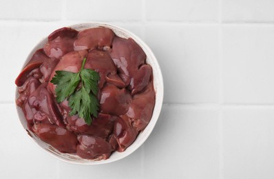 Bowl of raw chicken liver with parsley on white tiled table, top view. Space for text