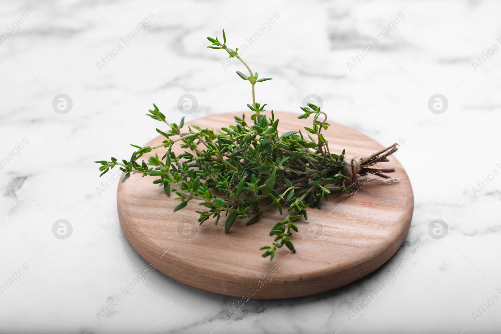 Photo of Board with aromatic fresh thyme on white marble table