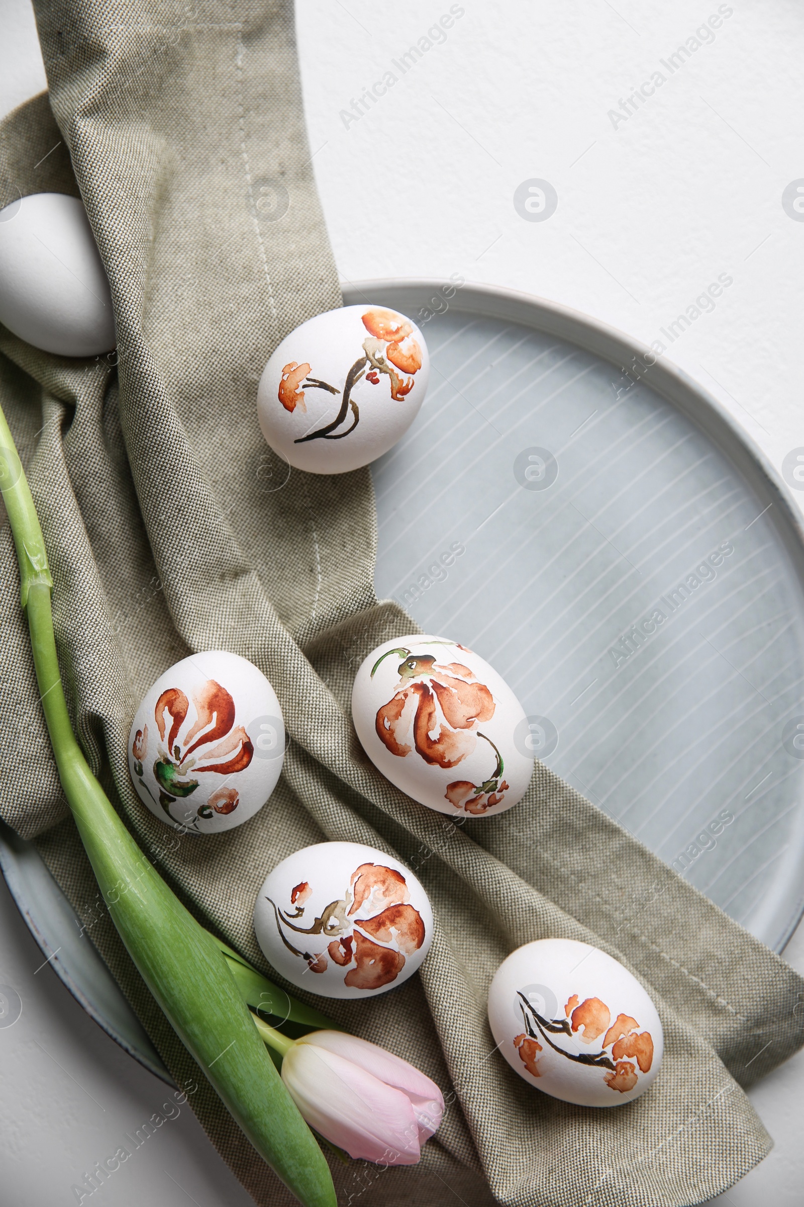 Photo of Beautifully painted Easter eggs and tulip on white table, top view