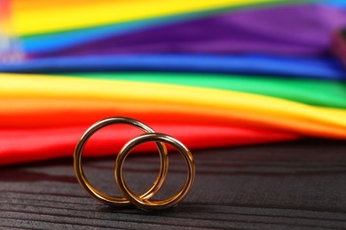 Rainbow LGBT flag and wedding rings on black wooden background, closeup