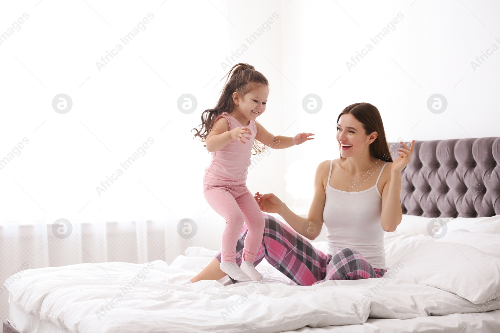 Photo of Happy mother with little daughter playing on bed