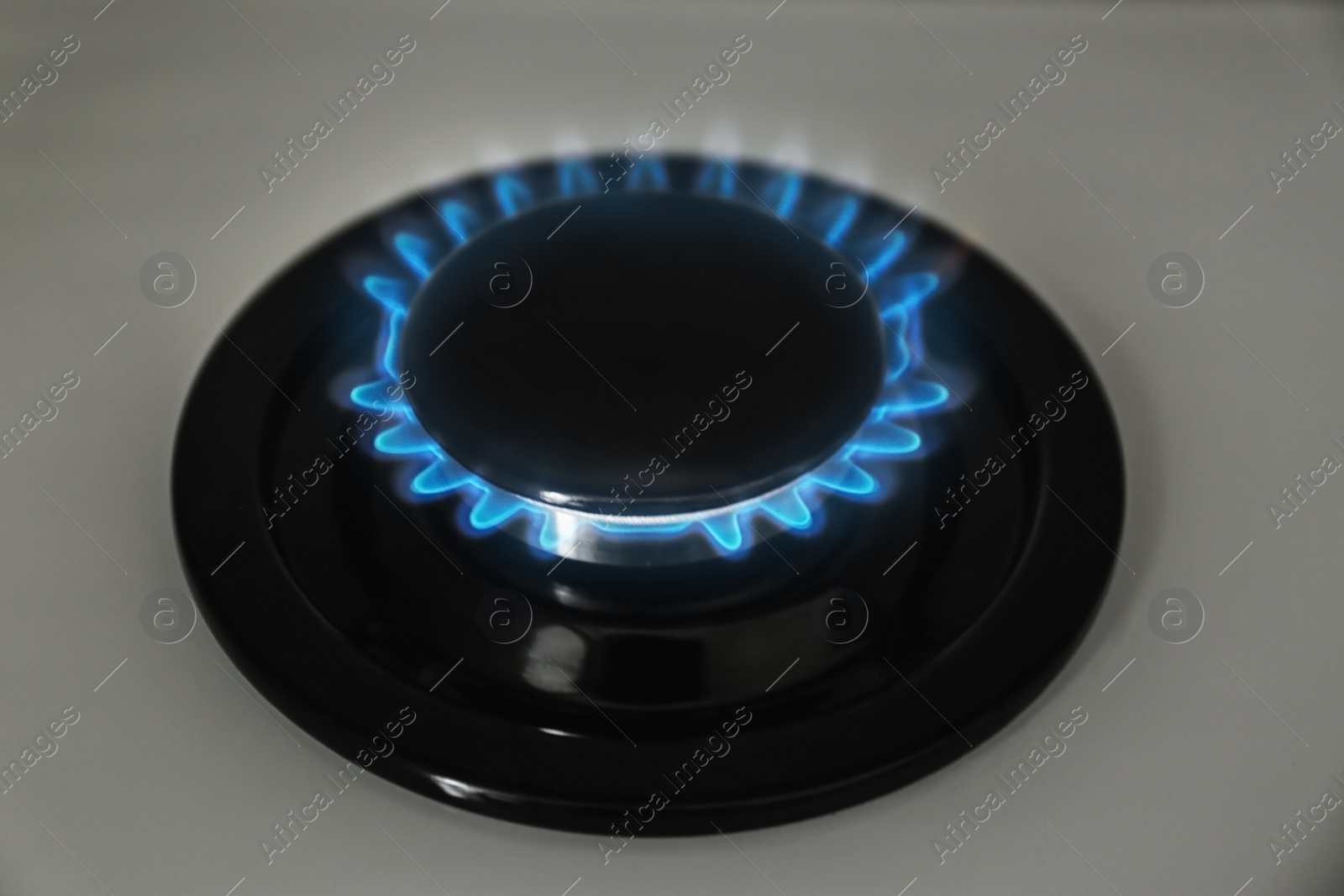 Photo of Gas burner with blue flame on modern stove, closeup