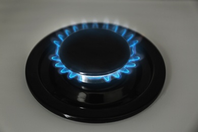 Gas burner with blue flame on modern stove, closeup