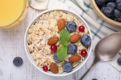 Photo of Oatmeal served with berries. almonds and mint on white table, flat lay