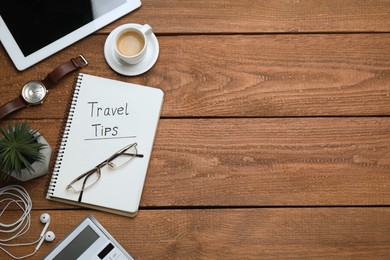 Photo of Notebook with phrase Travel Tips, cup of coffee and tablet on wooden table, flat lay. Space for text