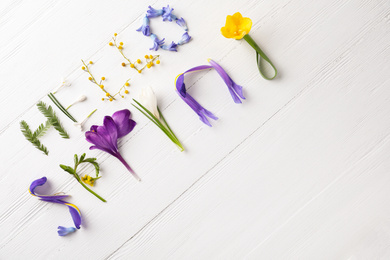 Photo of Words HELLO SPRING made of fresh flowers on white wooden table, flat lay. Space for text
