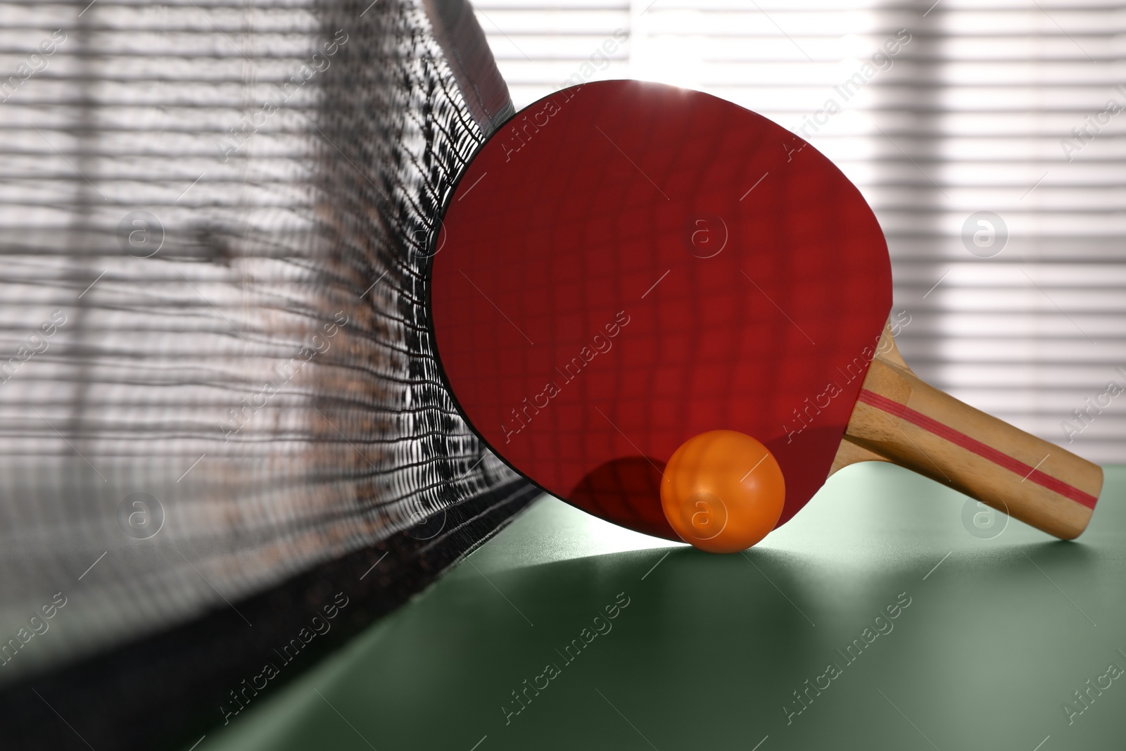 Photo of Racket and ball near net on ping pong table indoors