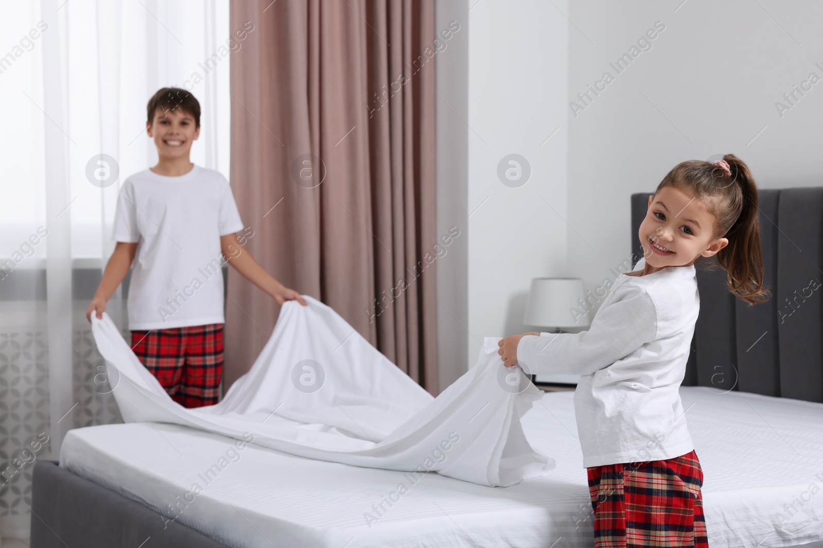 Photo of Brother and sister changing bed linens together in bedroom