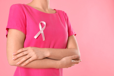 Woman with pink ribbon on color background, closeup. Breast cancer awareness