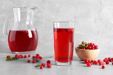 Tasty cranberry juice in glass and fresh berries on light grey table