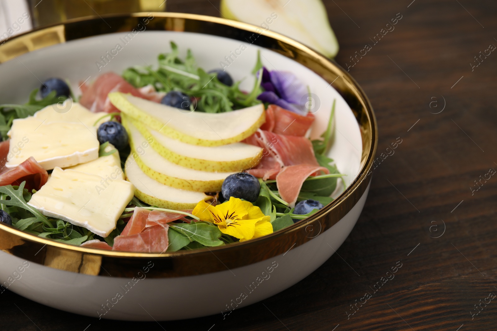 Photo of Tasty salad with brie cheese, prosciutto, blueberries and pear on wooden table, closeup