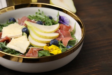 Photo of Tasty salad with brie cheese, prosciutto, blueberries and pear on wooden table, closeup