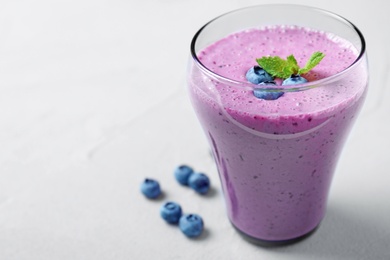 Glass of tasty blueberry smoothie on light grey table. Space for text