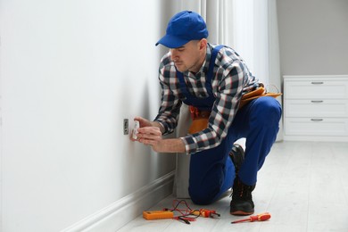 Professional male electrician repairing power socket in room