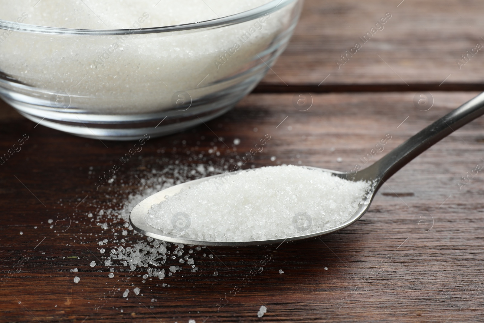 Photo of Granulated sugar in bowl and spoon on wooden table, closeup