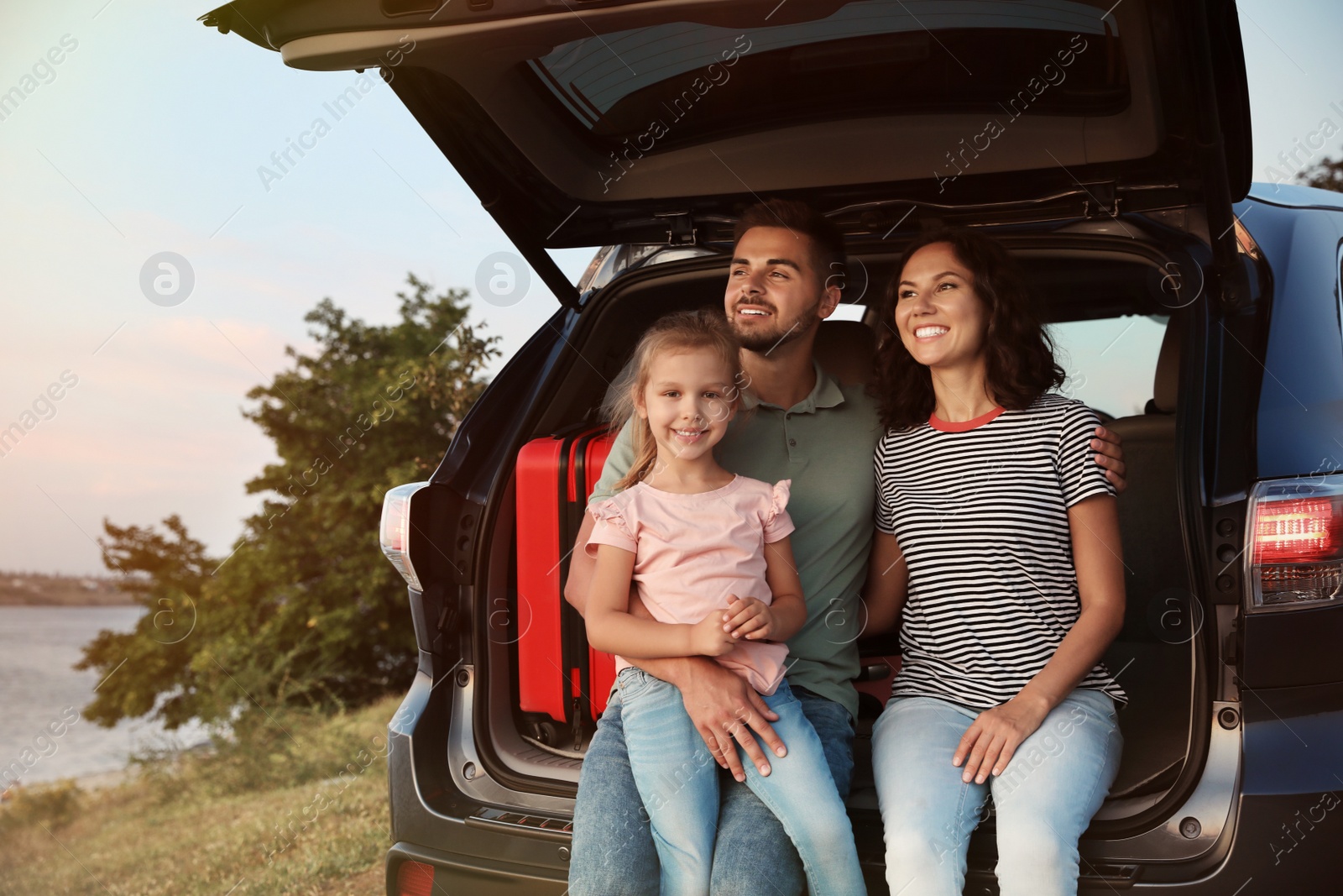 Photo of Happy young family sitting in car trunk on riverside