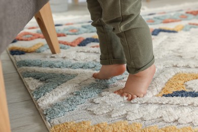 Baby standing on soft colorful carpet, closeup