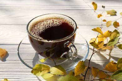 Photo of Cup of hot drink and leaves on white wooden table, closeup. Cozy autumn atmosphere