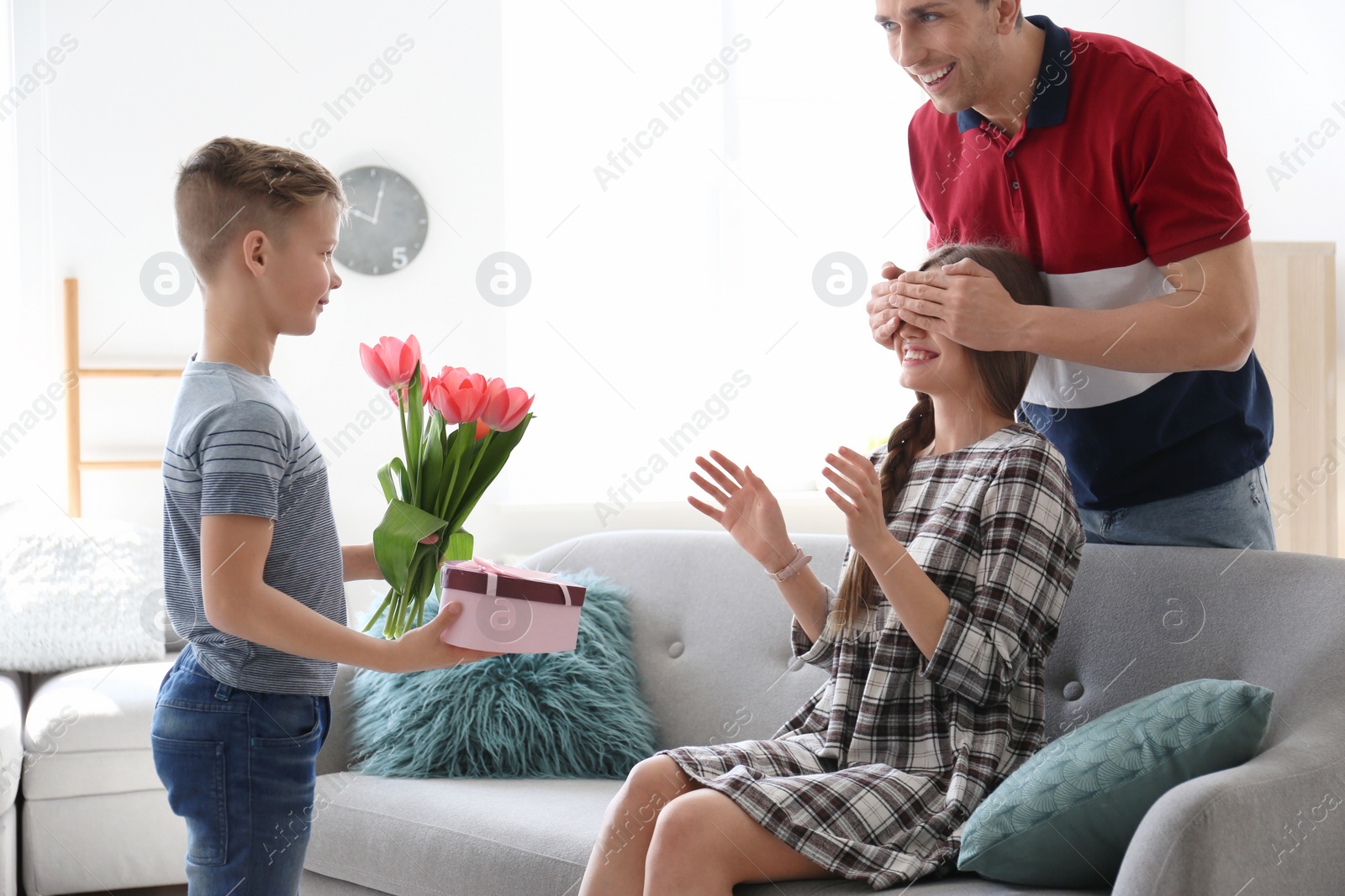 Photo of Happy woman receiving flowers and gift from her family at home. Mother's day celebration