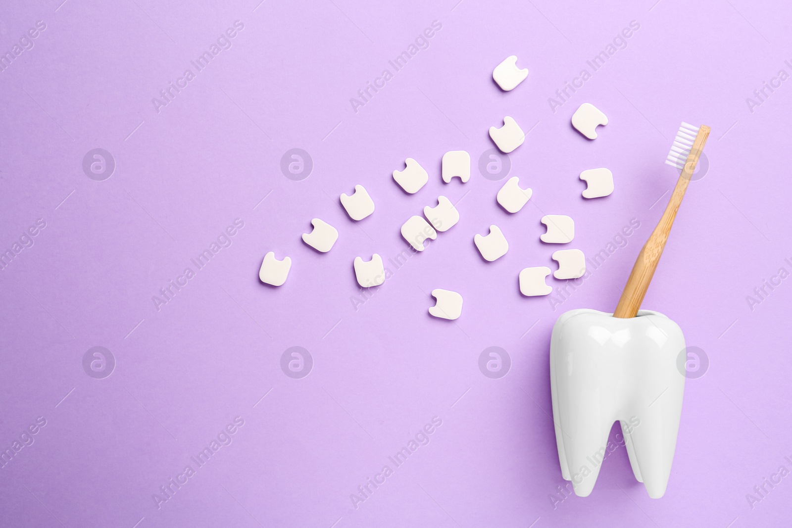 Photo of Small plastic teeth and wooden brush in holder on violet background, flat lay