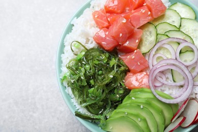 Photo of Delicious poke bowl with salmon, seaweed and vegetables on light grey table, top view