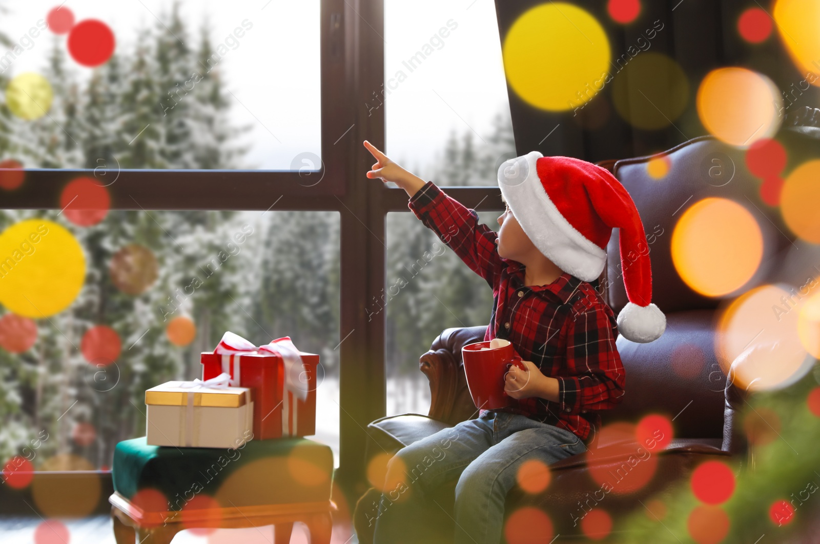 Photo of Little boy in Santa Claus cap near window indoors. Christmas holiday