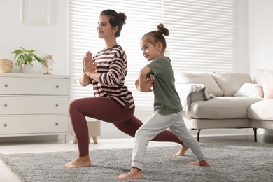 Young mother and her daughter practicing yoga together at home