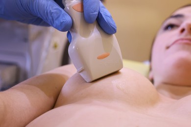 Mammologist conducting ultrasound examination of woman's breast in clinic, closeup