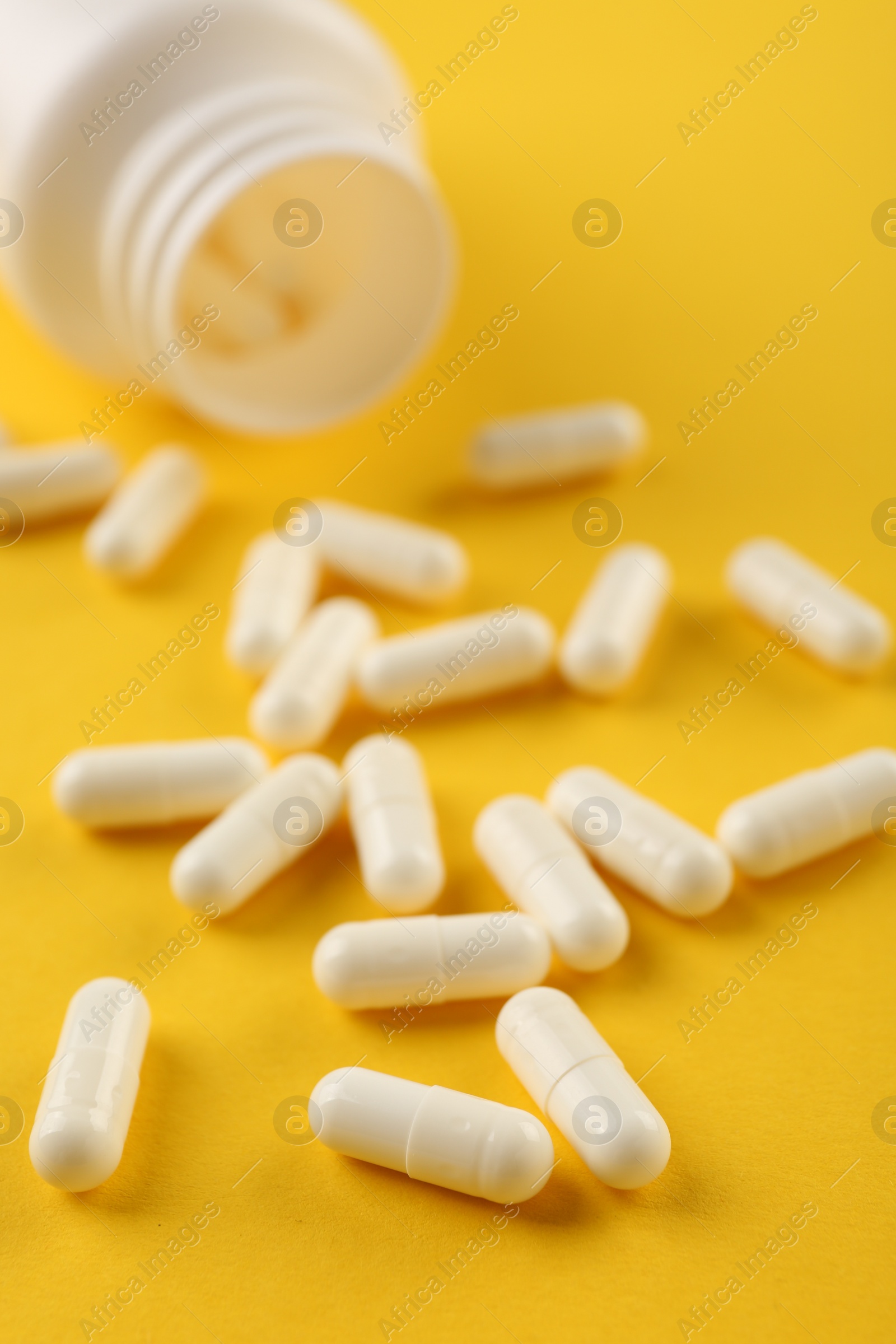 Photo of Bottle and vitamin capsules on yellow background, closeup