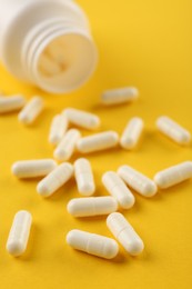 Photo of Bottle and vitamin capsules on yellow background, closeup