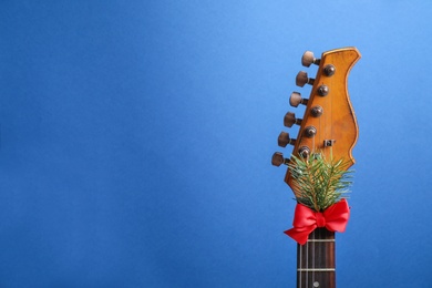 Photo of Guitar with red bow and fir branch on blue background, space for text. Christmas music