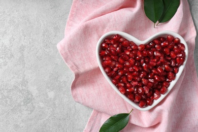 Photo of Heart shaped bowl of pomegranate seeds on grey background, top view with space for text