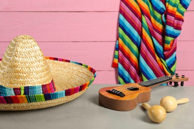 Mexican sombrero hat, maracas and ukulele on grey table, closeup