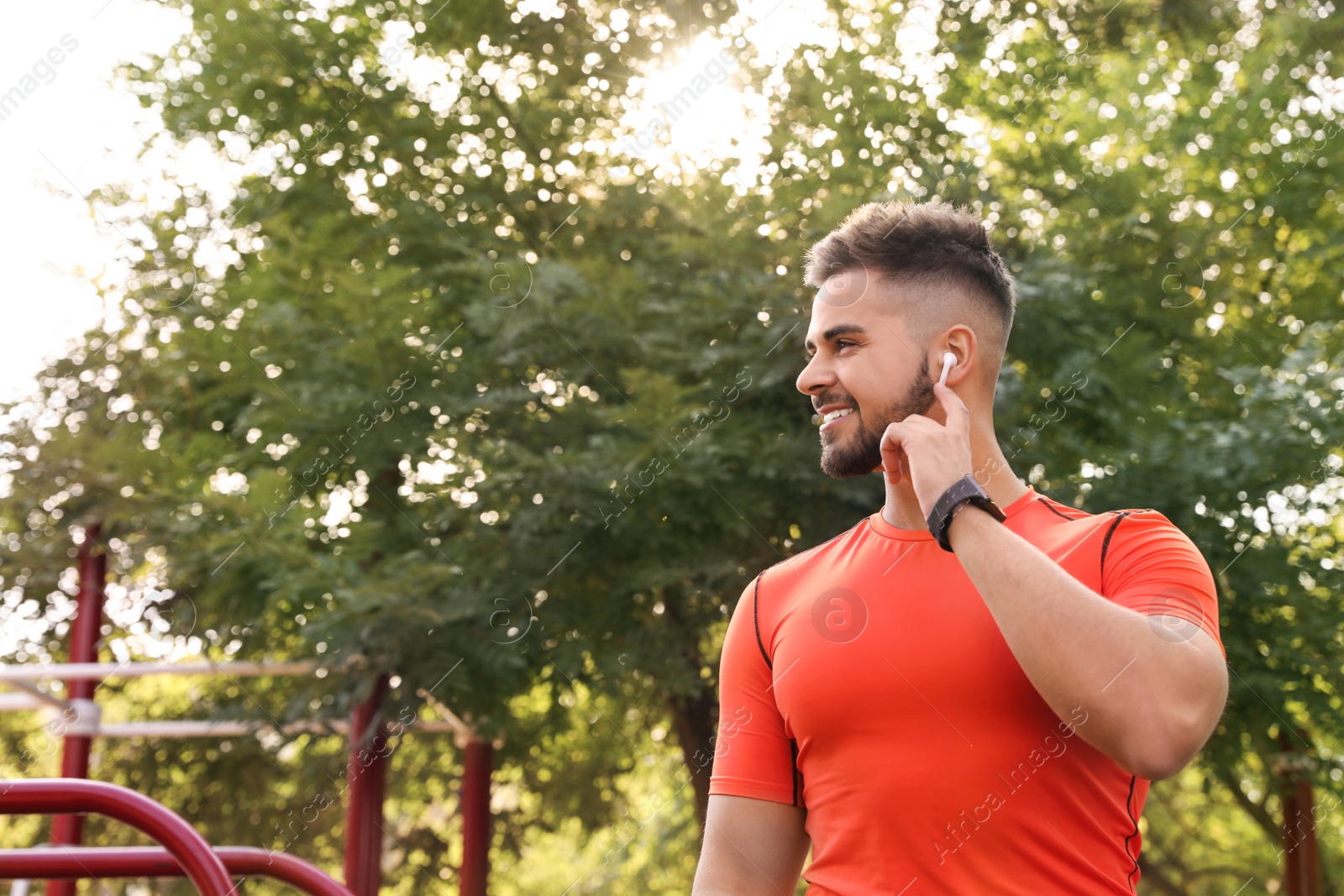 Photo of Young man with wireless headphones listening to music on sports ground. Space for text