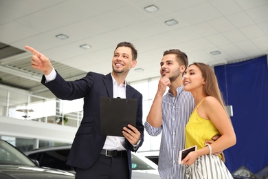 Young couple choosing new car with salesman in salon