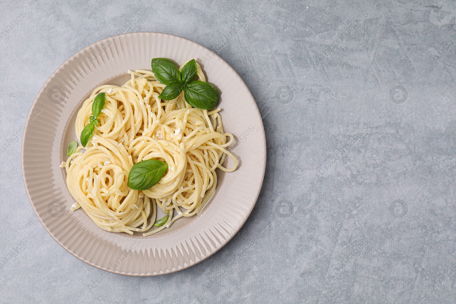 Photo of Delicious pasta with brie cheese and basil leaves on grey textured table, top view. Space for text
