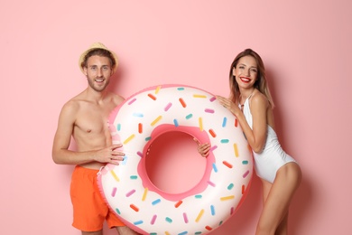 Photo of Happy young couple in beachwear with inflatable ring on color background