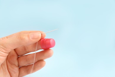 Photo of Woman with thimble, thread and sewing needle on light blue background, closeup. Space for text