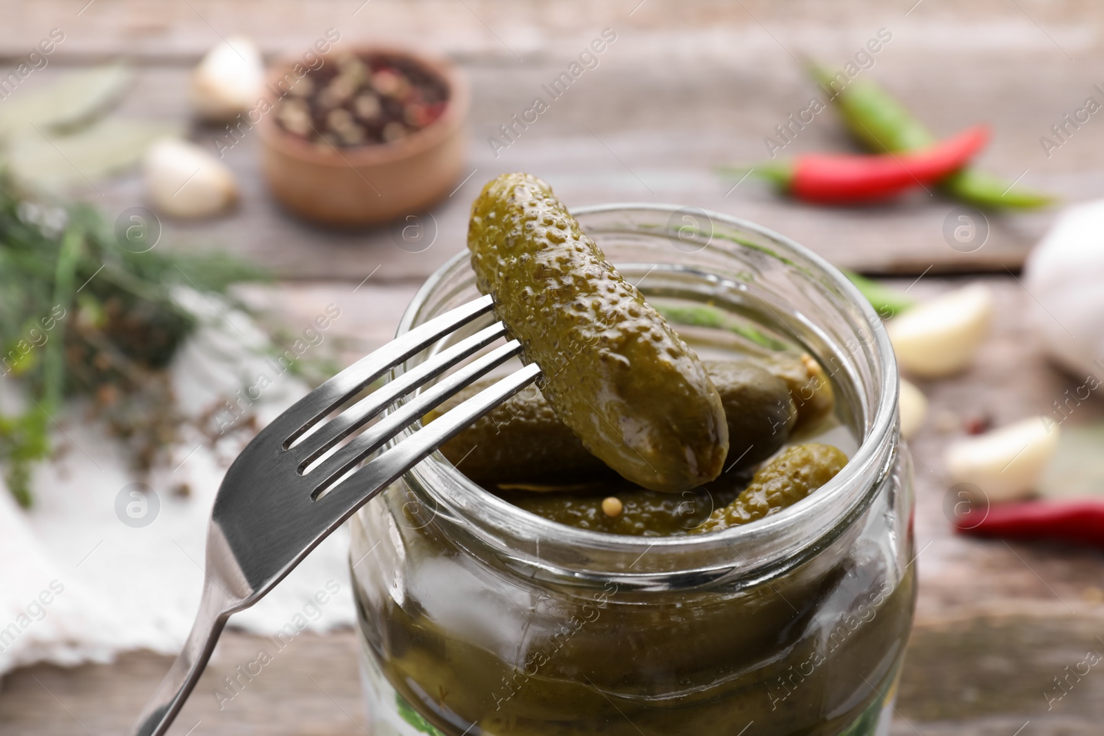 Photo of Fork with tasty pickled cucumber over jar on table, closeup