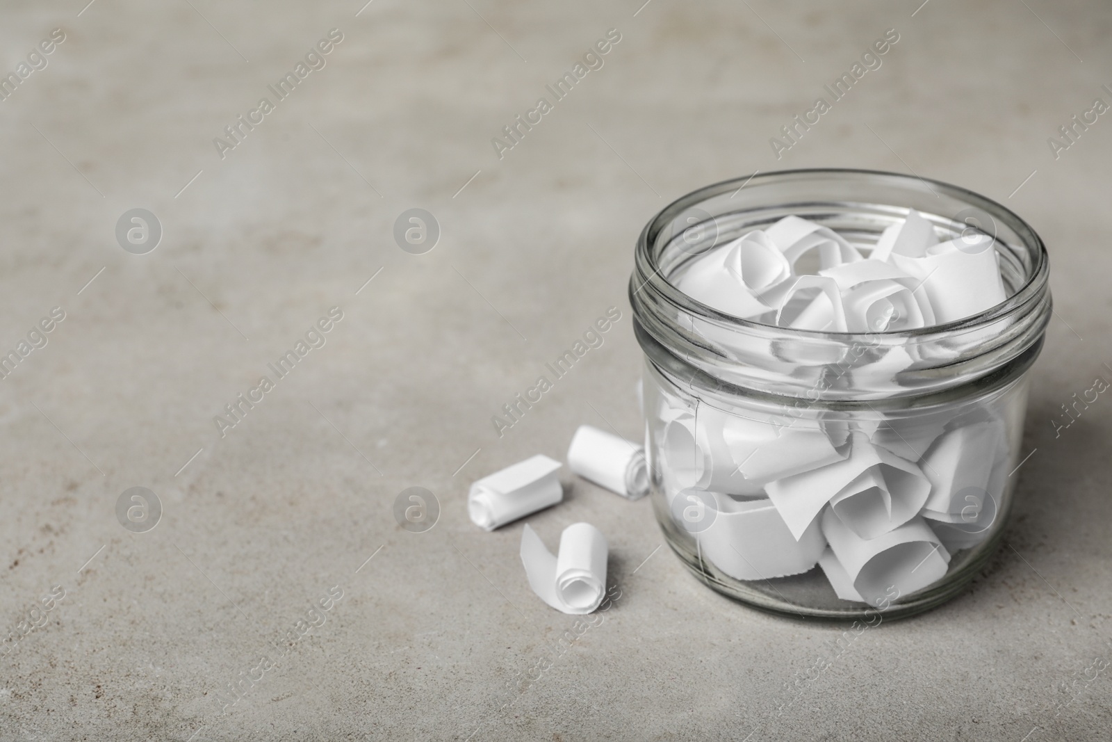 Photo of Glass jar with paper pieces on grey table, space for text