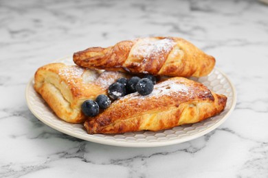 Fresh tasty puff pastry with sugar powder and blueberries served on white marble table, closeup
