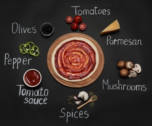 Pizza crust, ingredients and chalk written product's names on black background, flat lay