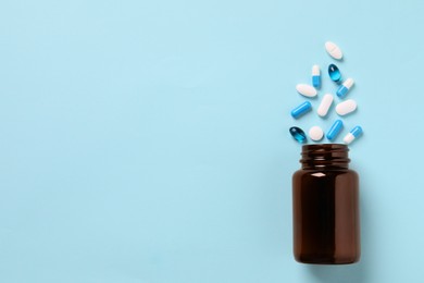 Plastic bottle with many different pills on light blue background, flat lay. Space for text