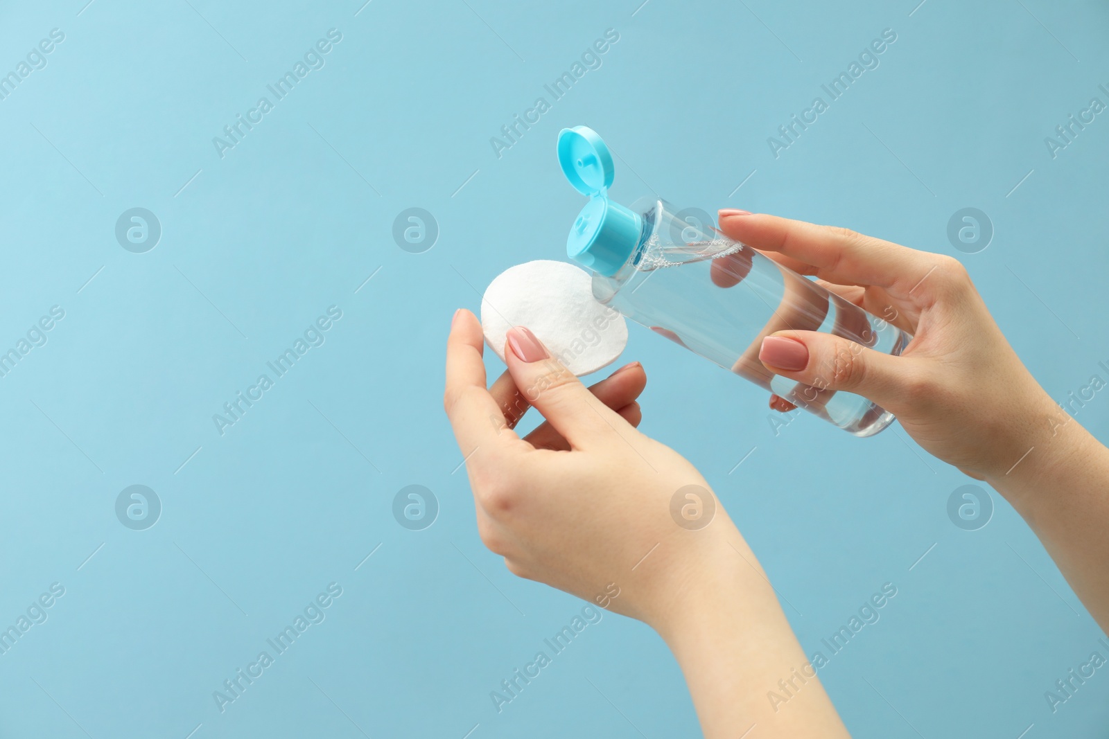 Photo of Woman pouring makeup remover onto cotton pad on light blue background, closeup. Space for text