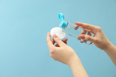 Woman pouring makeup remover onto cotton pad on light blue background, closeup. Space for text