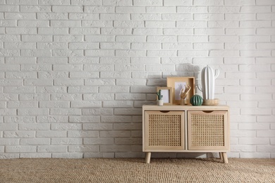 Photo of Stylish room interior with wooden cabinet near white brick wall. Space for text