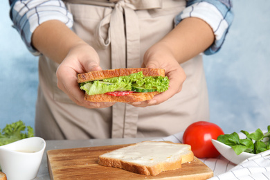 Photo of Woman holding tasty fresh sandwich at light grey marble table, closeup