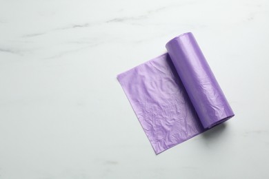 Photo of Roll of violet garbage bags on white marble table, top view. Space for text