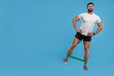 Young man exercising with elastic resistance band on light blue background. Space for text